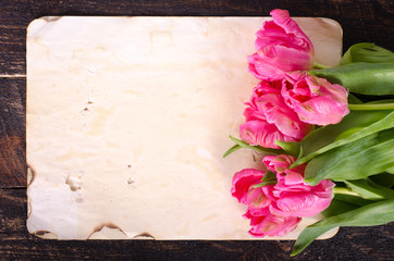 Pink tulips and princess shoes, vintage paper on wooden background. Free space for your text.