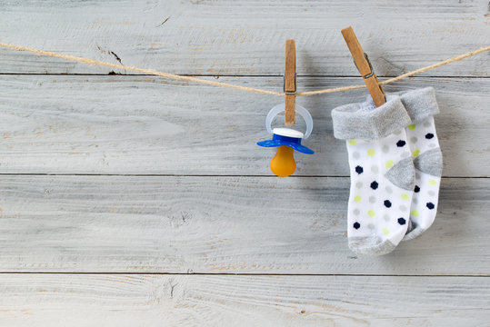 Baby pacifier and socks hanging on clothesline on wooden background