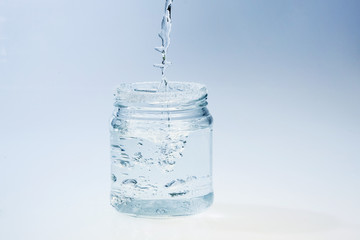 clean glass jar with pouring water againt light background