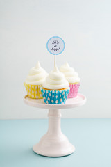 Three baby shower cupcakes for a boy with buttercream frosting on a cake stand