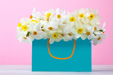 a bouquet of white daffodils in a blue package on wooden table on pink background