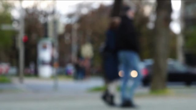 Unfocused blurred intersection with pedestrian walkway. People walking, bicyclists and inline skaters passing by, traffic light changing colors.