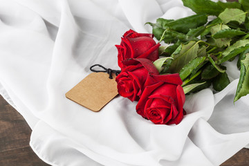 Three red roses with gift tag on silk folds with copy space. Elegant women's day present. Shallow depth of field