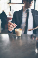 Hand of businessman stirring coffee in cafe while reading newspa