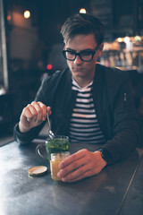 Hipster man with retro glasses putting honey in fresh mint tea
