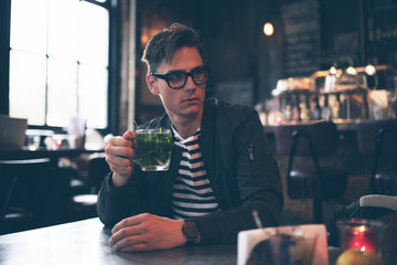 Fashionable man with retro glasses having fresh mint tea in cafe