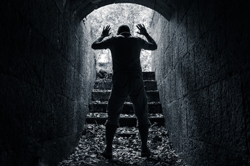 Man leaves dark stone tunnel with raised hands