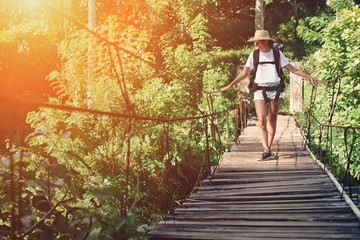 Young woman with backpack and hat traveling over hanging bridge (intentional sun glare)