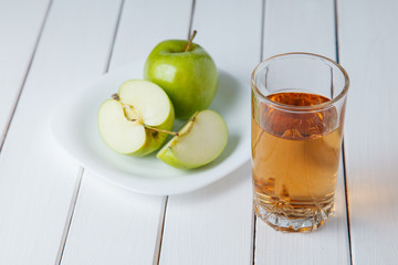 Glass of apple juice and apples on wooden table, on nature background