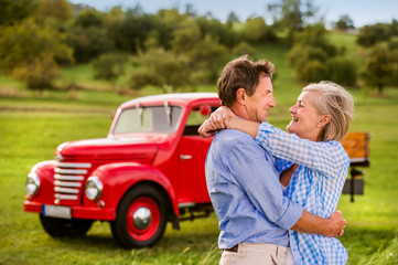 Senior couple hugging, vintage styled red car, sunny nature