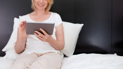 Woman sitting on bed using digital tablet