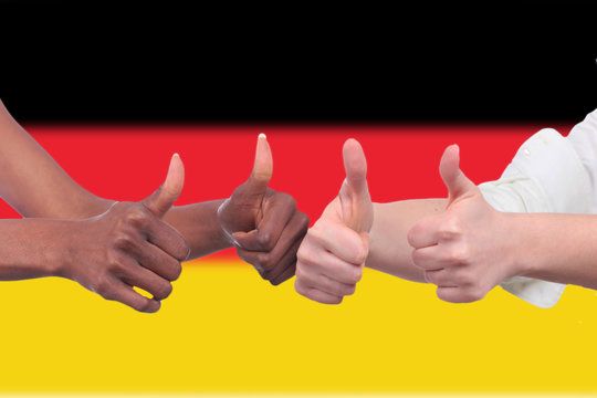 Weiße und schwarze Hände halten Daumen hoch vor Deutschland Fahne