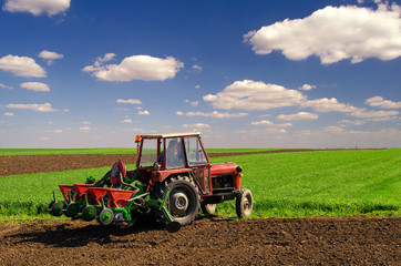 Farmer with tractor sowing on agricultural fields on sunny spring