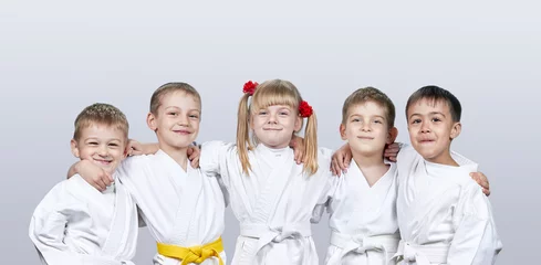 Fotobehang Vechtsport Vrolijke kinderen in karategi op een grijze achtergrond