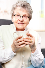 Starsza pani pije napar z ziół. Starsza kobieta odpoczywa na fotelu z kubkiem naparu z ziół - obrazy, fototapety, plakaty