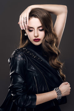 Glamorous young beautiful rock style girl in black leather jacket with accessories on dark gray background