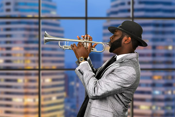 Afro trumpeter in black hat. Trumpet performance on skyscraper background. Reggae music for your pleasure. Classy musician on stage.