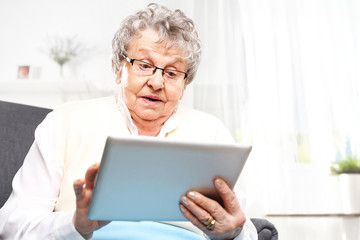 Zdziwiona starsza kobieta patrzy w ekran tabletu.