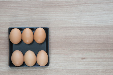Six eggs in black plate on wooden surface with space for text