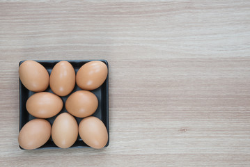Eight eggs in black plate on wooden surface with space for text