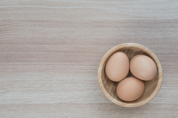 Three eggs in wooden bowl on wooden surface