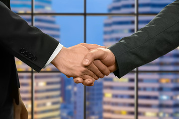 Caucasian businessmen shaking hands. Managers shake hands beside skyscraper. Productive day at...