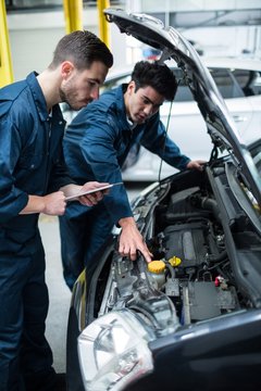Mechanics examining car engine using digital tablet