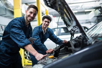 Mechanics examining car engine using digital tablet