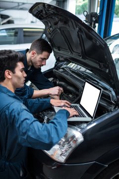 Mechanics examining car engine using laptop