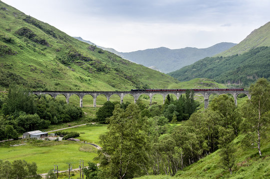 Glenfinnan, Scotland - - July 11, 2015: Viaduct with train and mountains in the background. The spot became famous through movies such as Harry Potter.