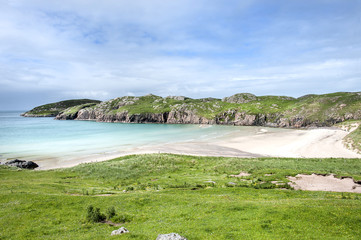 Scotland: White beach of Scourie bay with green grass and rocky cliffs