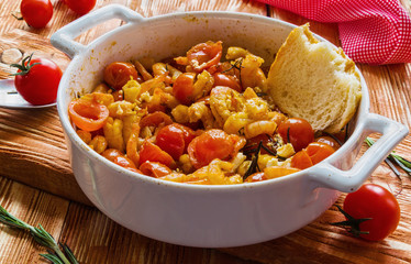 Shrimps in white baking dish on wooden background. Baked with cherry tomatoes and feta cheese.