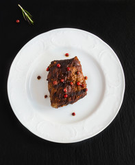 Big beef steak on white plate on black slate background. Top view.