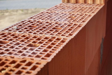 Row of red bricks with the inner holes in the shape of honeycomb on the construction site 