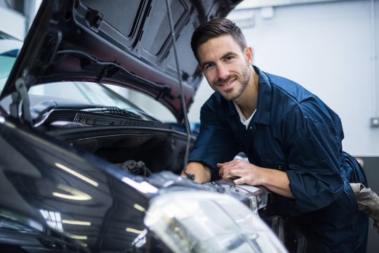 Portrait of smiling mechanic while examining car engine