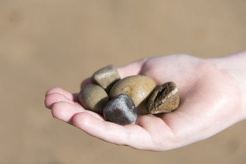 Close up image of a young boys hand holding pebbles on the beach 