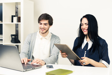 Obraz premium Two young people working together with laptop and tablet while sitting at minimalistic white office