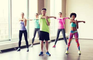 group of smiling people stretching in gym