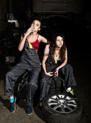 Fototapeta na wymiar tired mechanics sexy girls sitting on a pile of tires on a car repairs, one of the girls smoke. colorless life concept