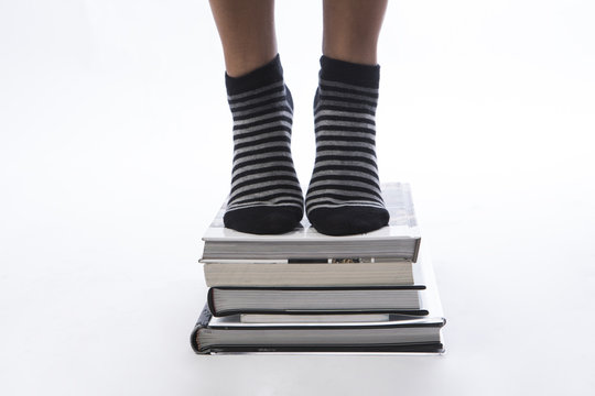 Dettaglio di piedi femminili con calze a righe in punta se dei libri  accatastati - sfondo bianco