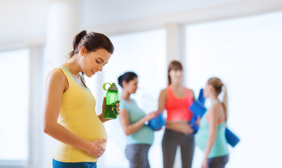 happy pregnant woman with water bottle in gym