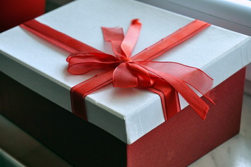 
Red and white gift box with a scarlet ribbon on the top in a shape of great topknot 
