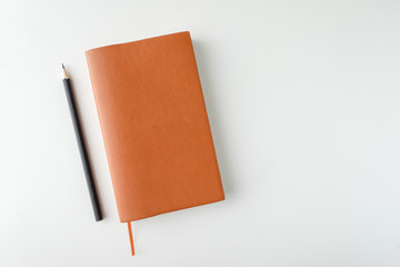top view blank orange leather diary and pencil on white desk