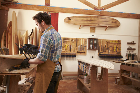 Carpenter Glueing Bespoke Wooden Surfboard In Workshop