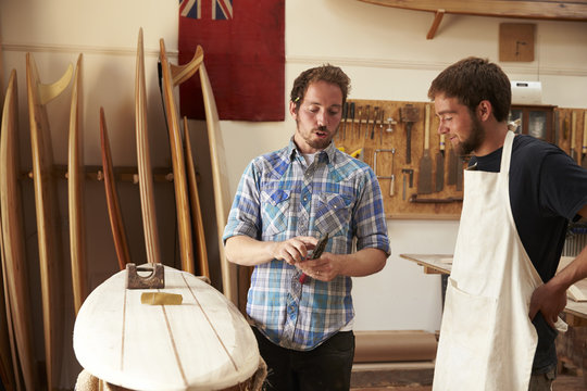 Carpenter With Apprentice Making Bespoke Wooden Surfboard