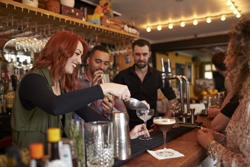 Woman Learning How To Mix Cocktail At Lesson In Bar