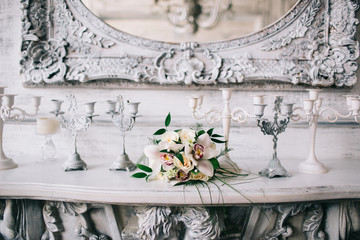 Bridal bouquet of lilies lies on the fireplace in the Palace. Next candle stand. Against the backdrop of ancient mirrors