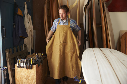Carpenter Putting Apron On In Bespoke Surfboard Workshop - Powered by Adobe