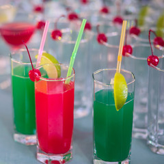 Beautiful row line of different colored alcohol cocktails with mint on a tropical Hawaiian hawaii style party, martini, vodka,and others on decorated catering bouquet table on open air beach event