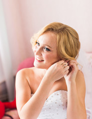 Naklejka premium Beautiful elegant bride putting on earrings closeup, wedding preparation.